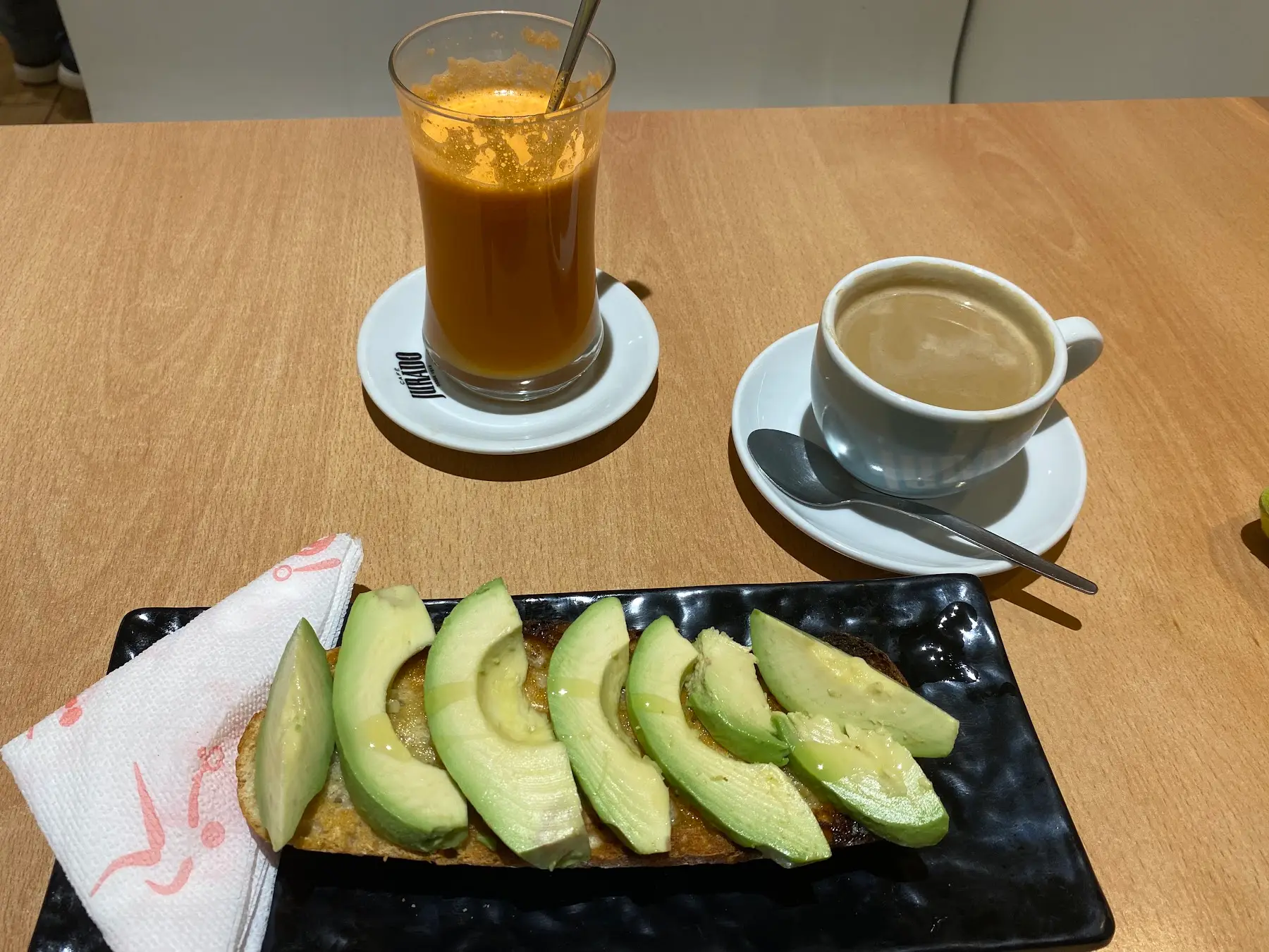Tostada con aguacate en una tabla negra, un zumo natural y un café